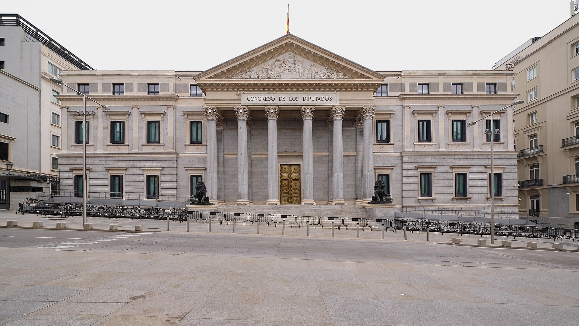 The neoclassical facade of Spain's Congress of Deputies in Madrid, with columns, bronze lions and a Spanish flag on the roof