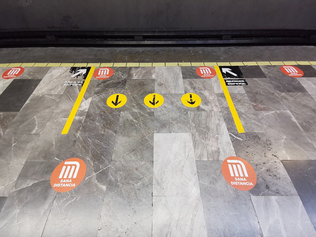 Orange Mexico City Metro stickers reading Sana distancia and black arrows marked Área de espera on a station platform floor
