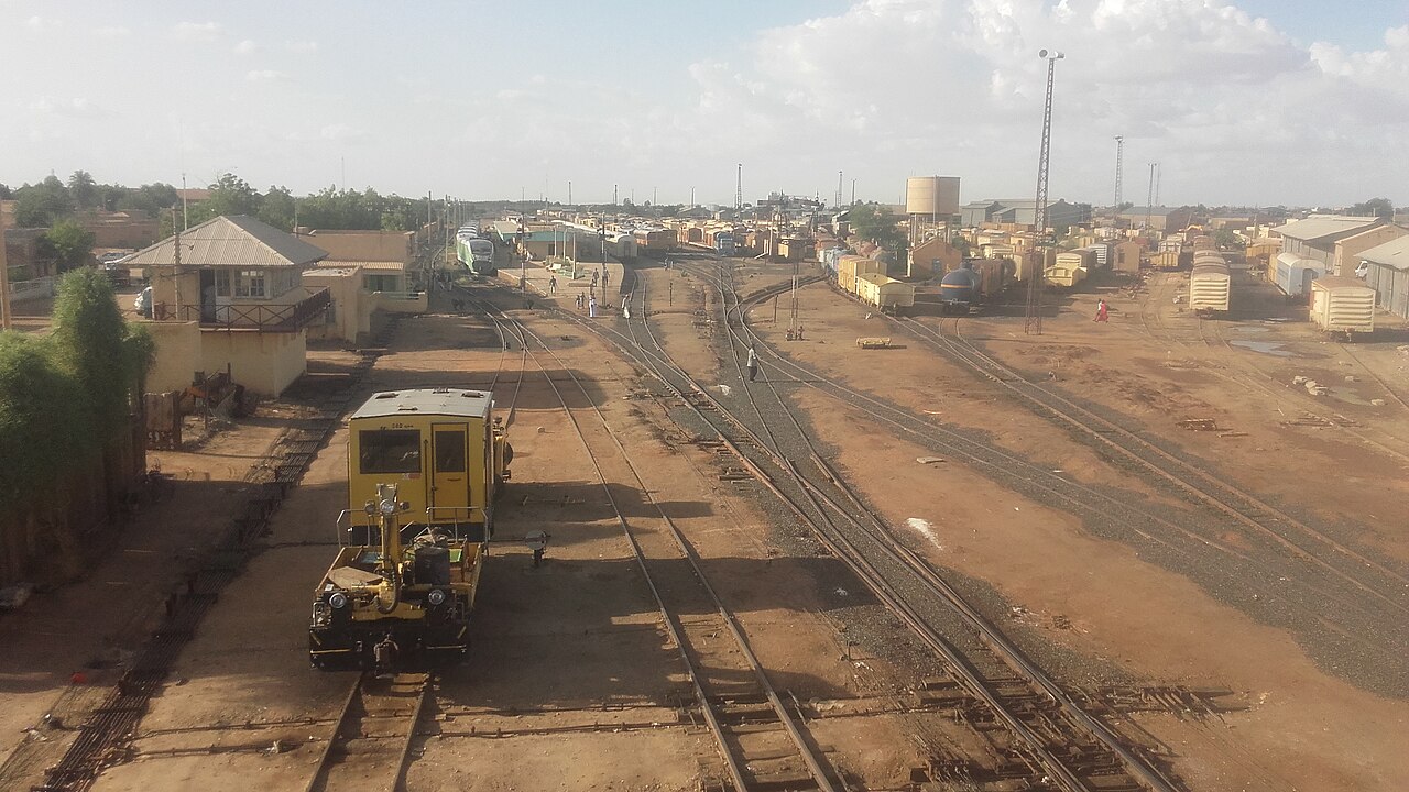 Railway tracks, a yellow track vehicle and station buildings at Atbara City railway station in Sudan