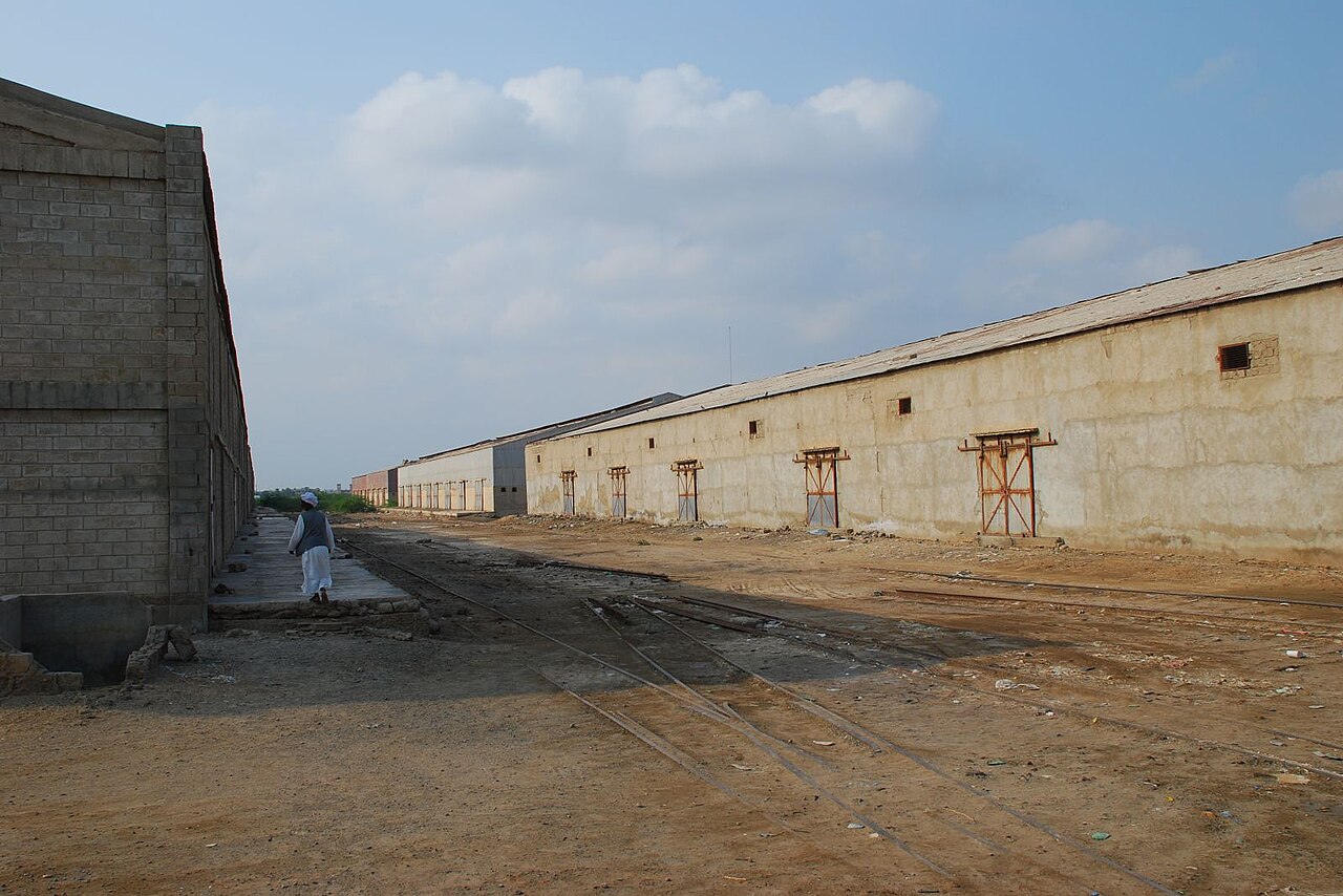 Long storage warehouses with rail tracks in front, north of the harbour in Port Sudan, with a man in white robes walking past