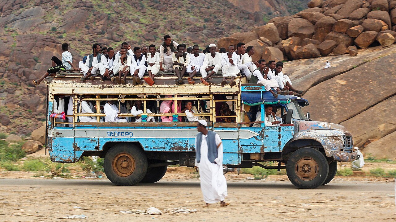 A crowded blue bus with passengers on the roof drives past rocky hills near Kassala in eastern Sudan.