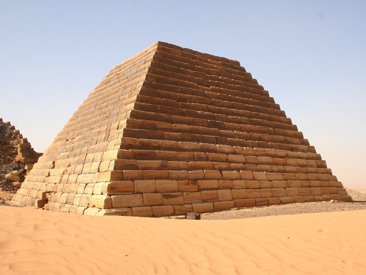 A stepped sandstone pyramid at the Meroe site in the Sudanese desert under a clear sky