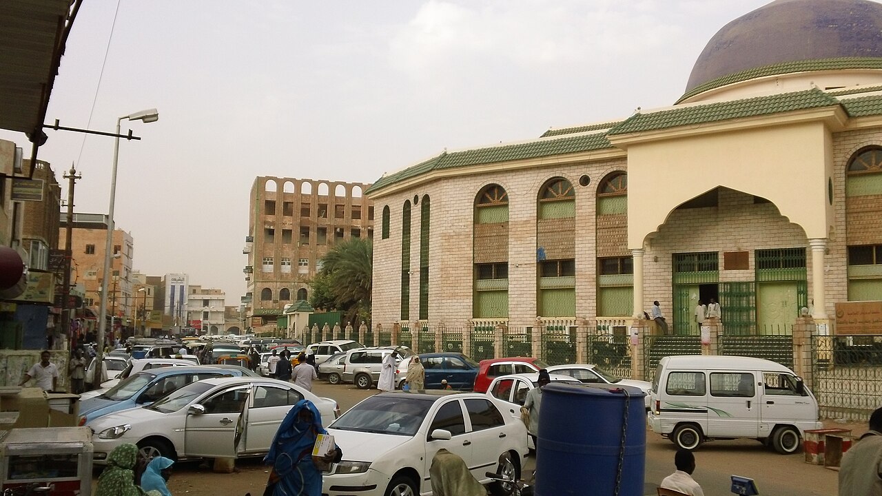 Cars and pedestrians on a busy street beside a domed mosque in Omdurman, Sudan