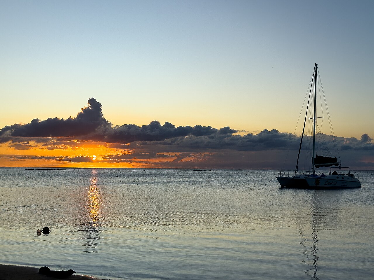 Sunset over the sea at Mont Choisy beach in Mauritius with a sailing catamaran at anchor