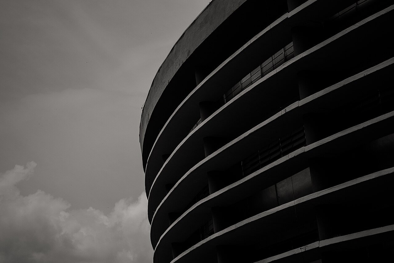 Black-and-white close-up of the curved, ringed concrete facade of Ginásio do Ibirapuera in São Paulo under a cloudy sky.