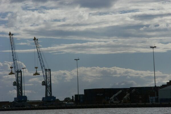 Container cranes and stacked shipping containers at the port of Paramaribo, Suriname, under a cloudy sky
