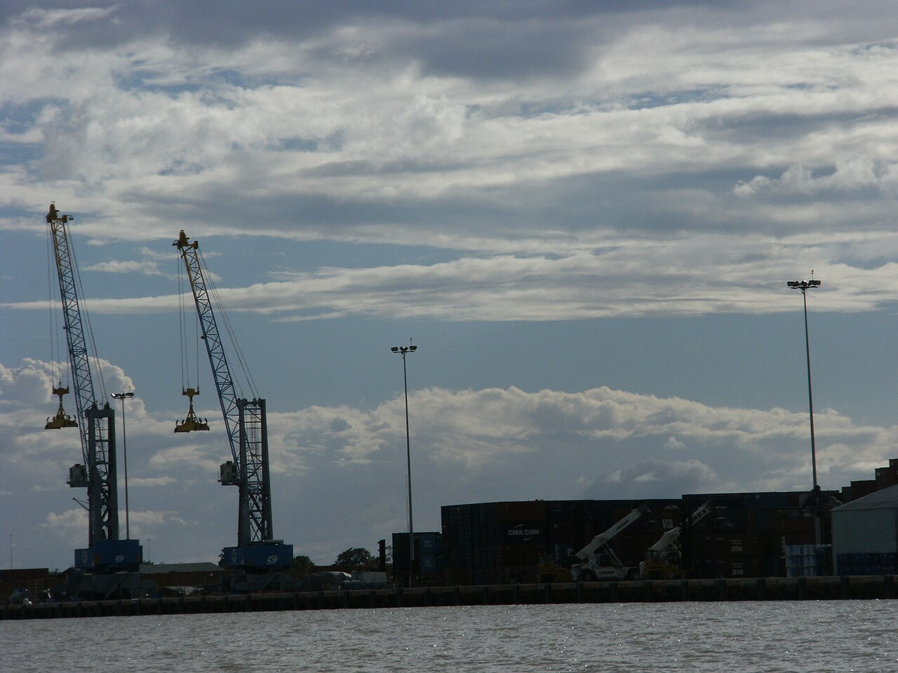 Container cranes and stacked shipping containers at the port of Paramaribo, Suriname, under a cloudy sky
