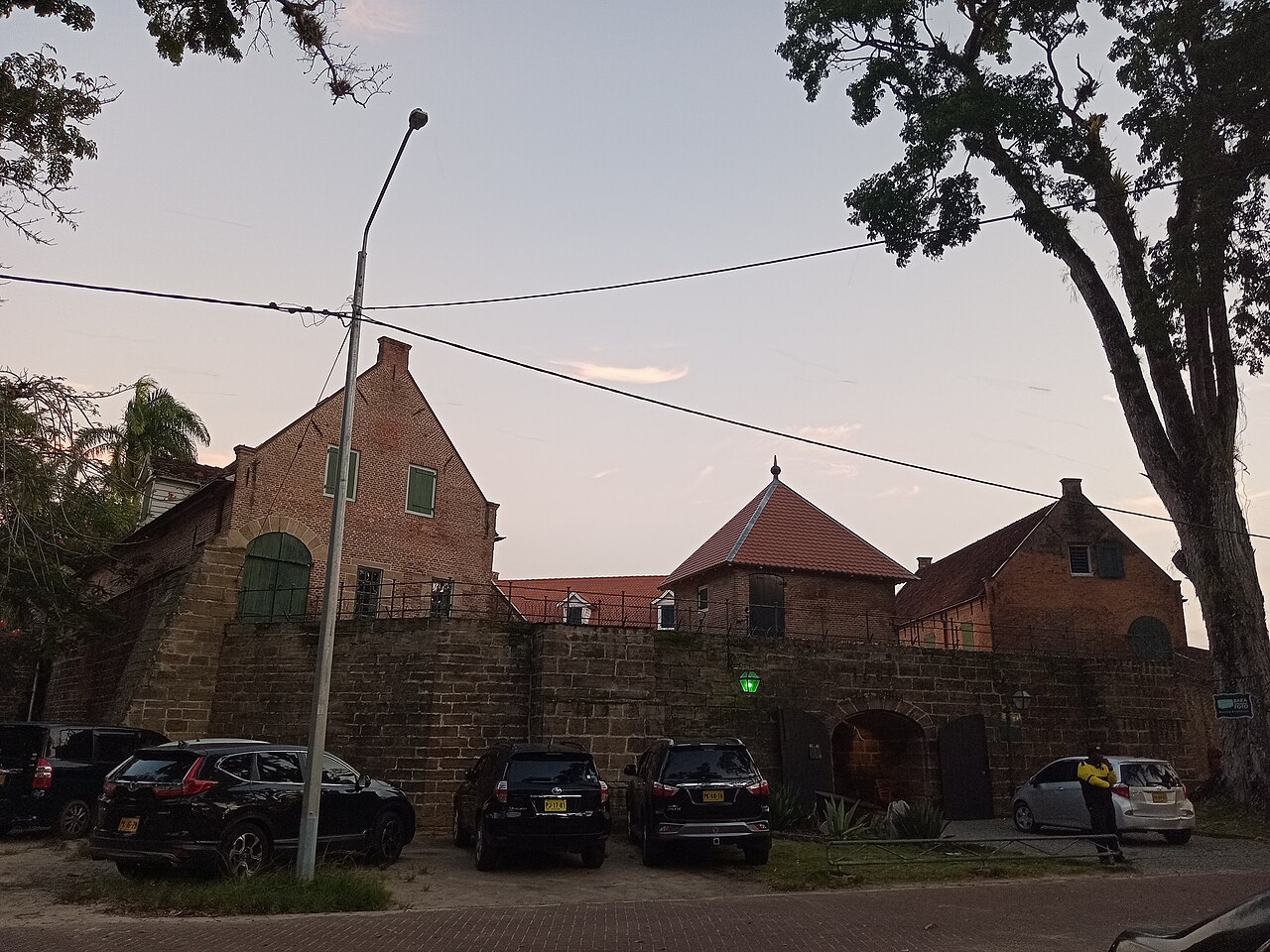Brick gables and stone walls of Fort Zeelandia in central Paramaribo at dusk, with parked cars in front