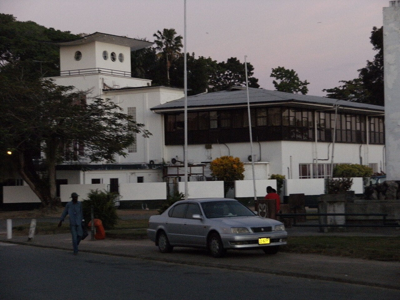 The older white National Assembly building in Paramaribo at dusk, with a tower with round windows and a dark-windowed upper floor.