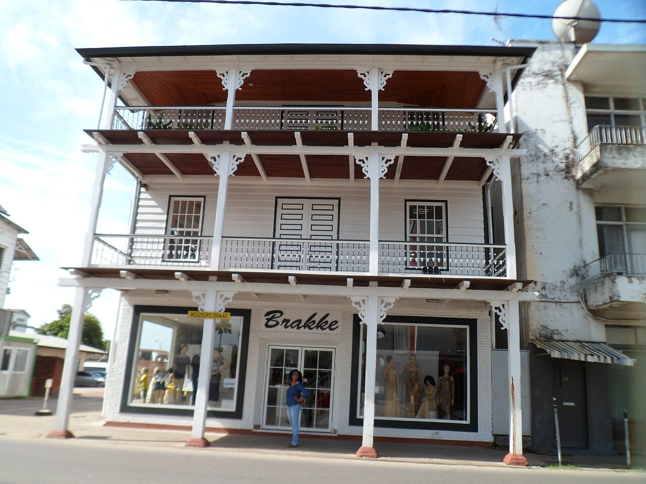 White three-storey wooden building with balconies and a clothing shop on the ground floor, under a yellow Keizerstraat street sign in Paramaribo