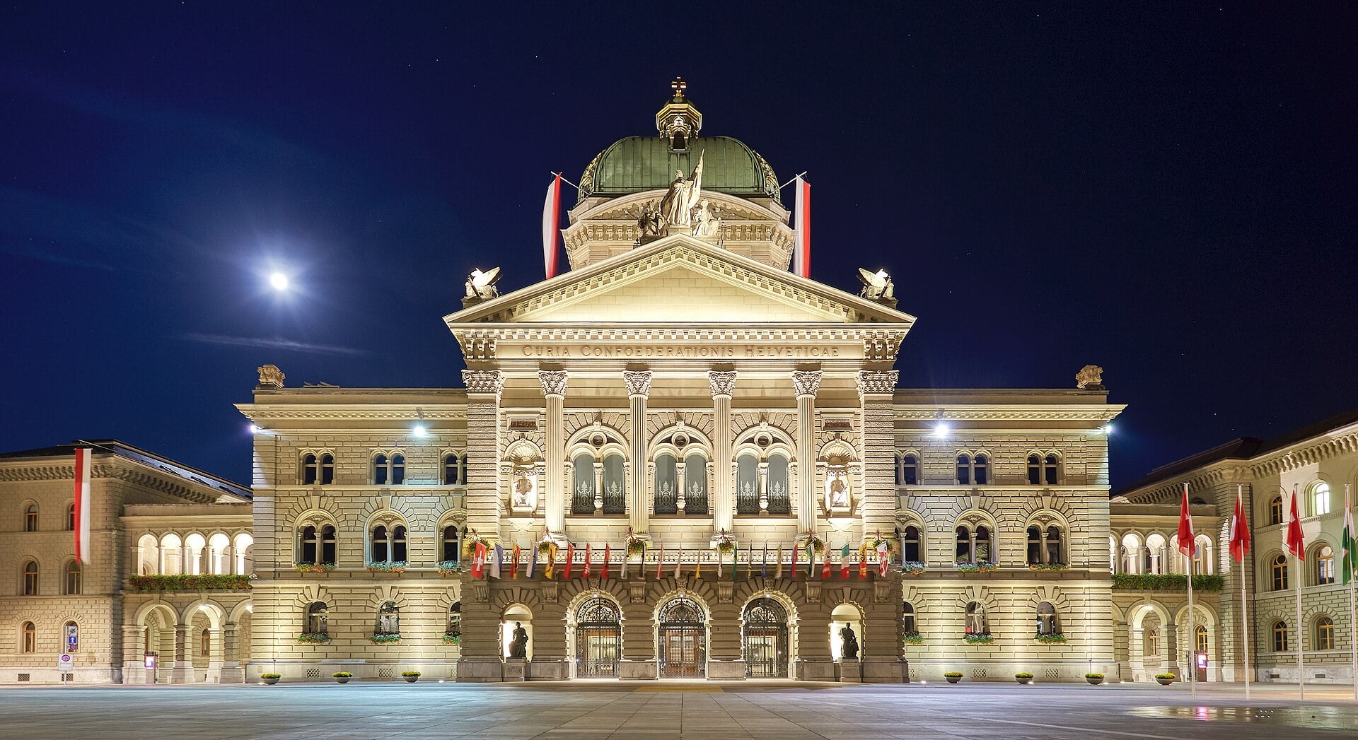 The Federal Palace in Bern, seat of the Swiss government and parliament, lit at night with flags on Bundesplatz