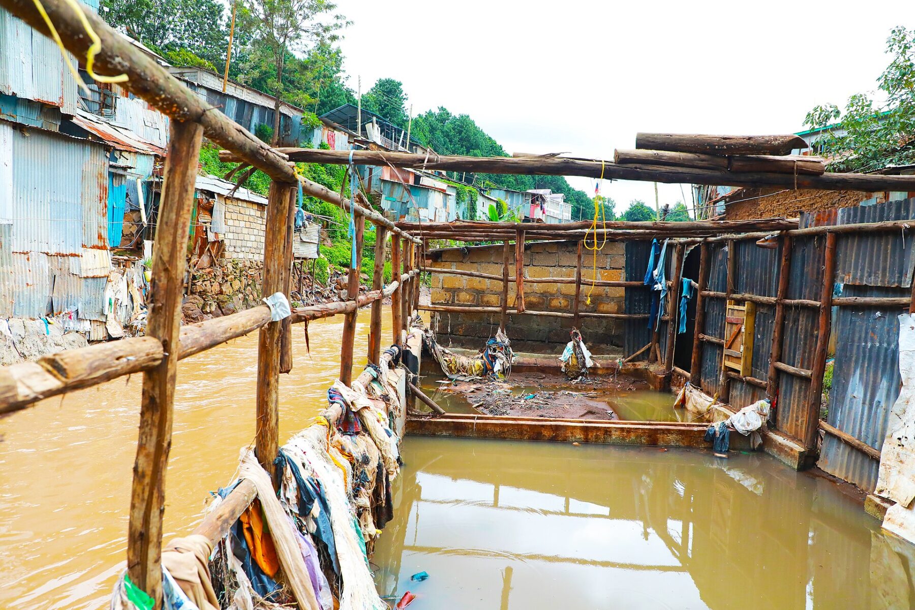 Brown floodwater fills a channel between iron-sheet homes and wooden walkways in Kibra, Nairobi