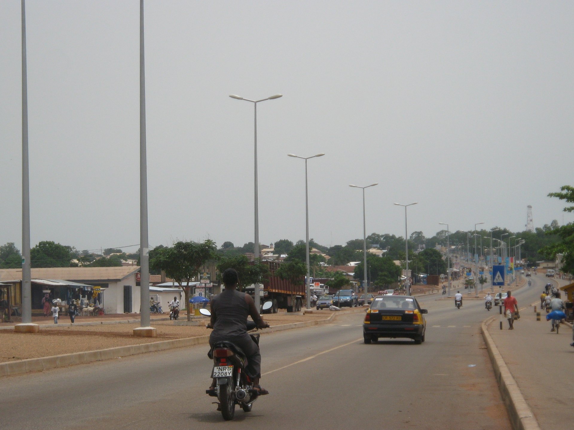 Motorbikes and cars on a main road lined with street lights in Tamale, Ghana