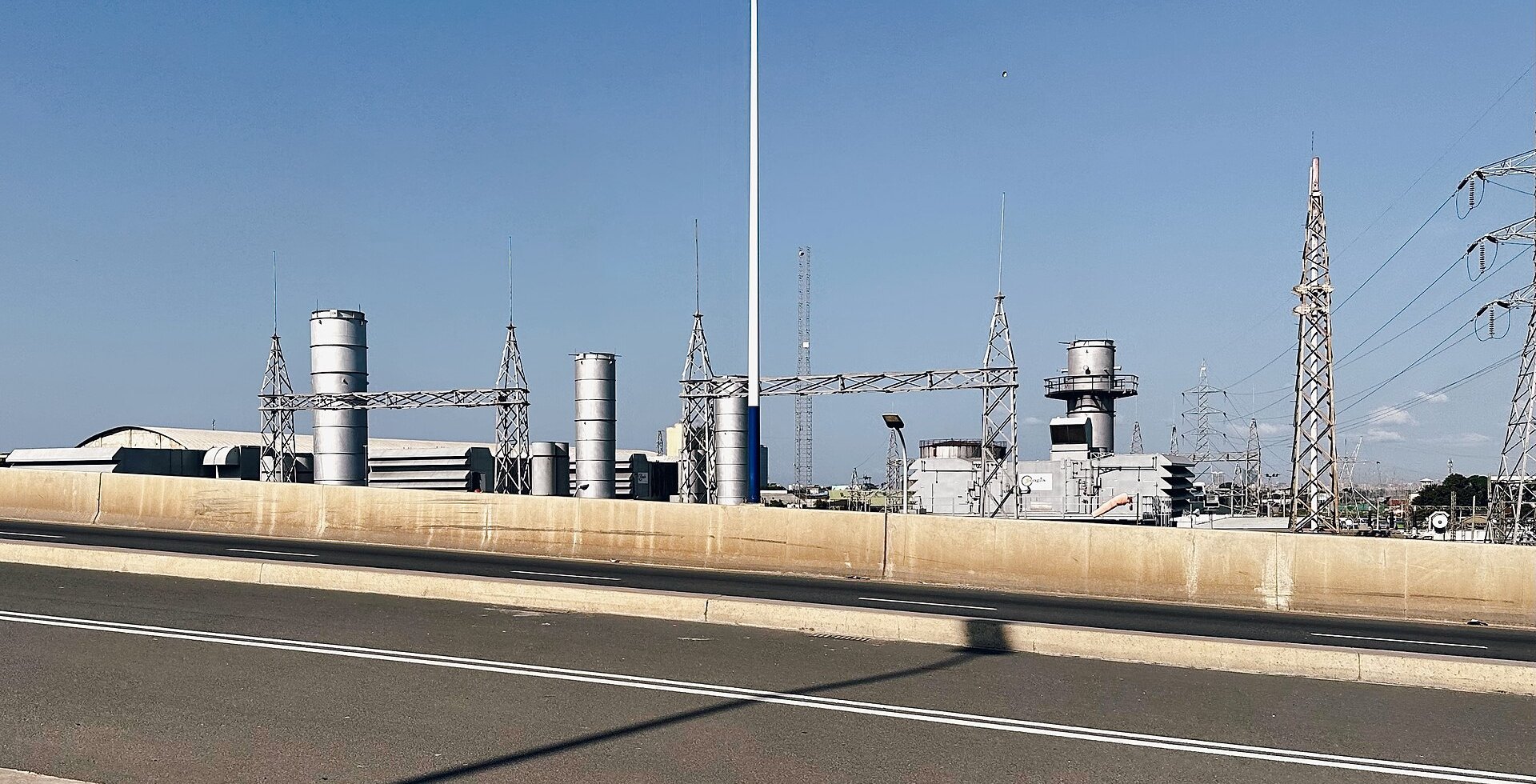 Power plant with silver exhaust stacks and high-voltage pylons beside a flyover in Dar es Salaam