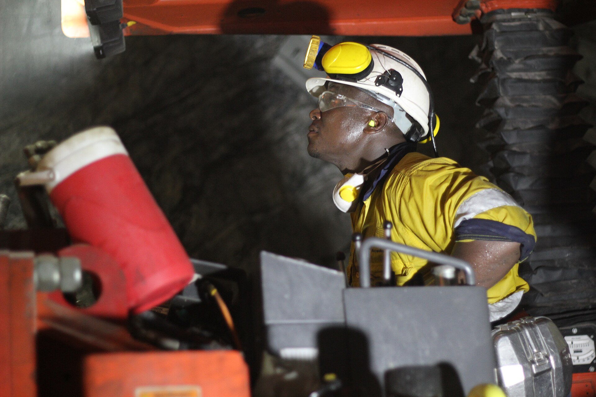 Worker in a hard hat and yellow overalls operating a drilling machine underground at the Shanta Gold mine in Tanzania