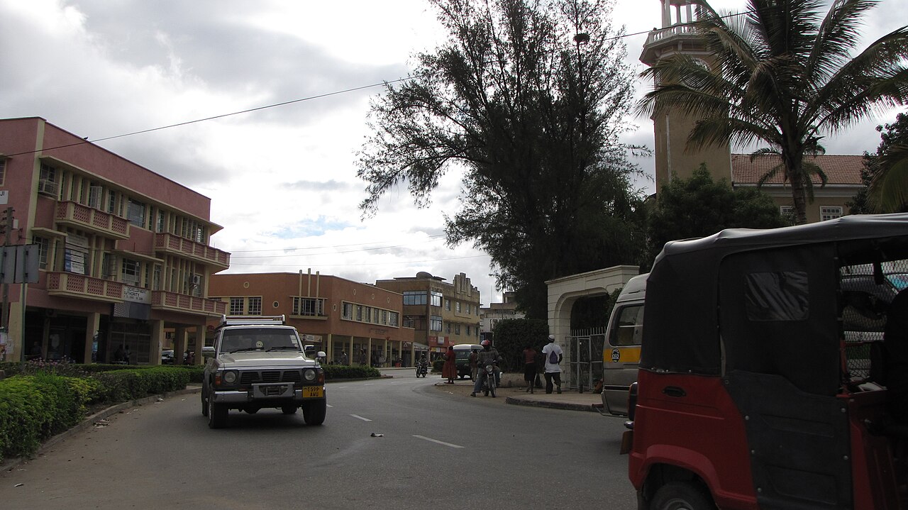 Street in central Dodoma, Tanzania, with shops, a clock tower, a car and a motorised rickshaw