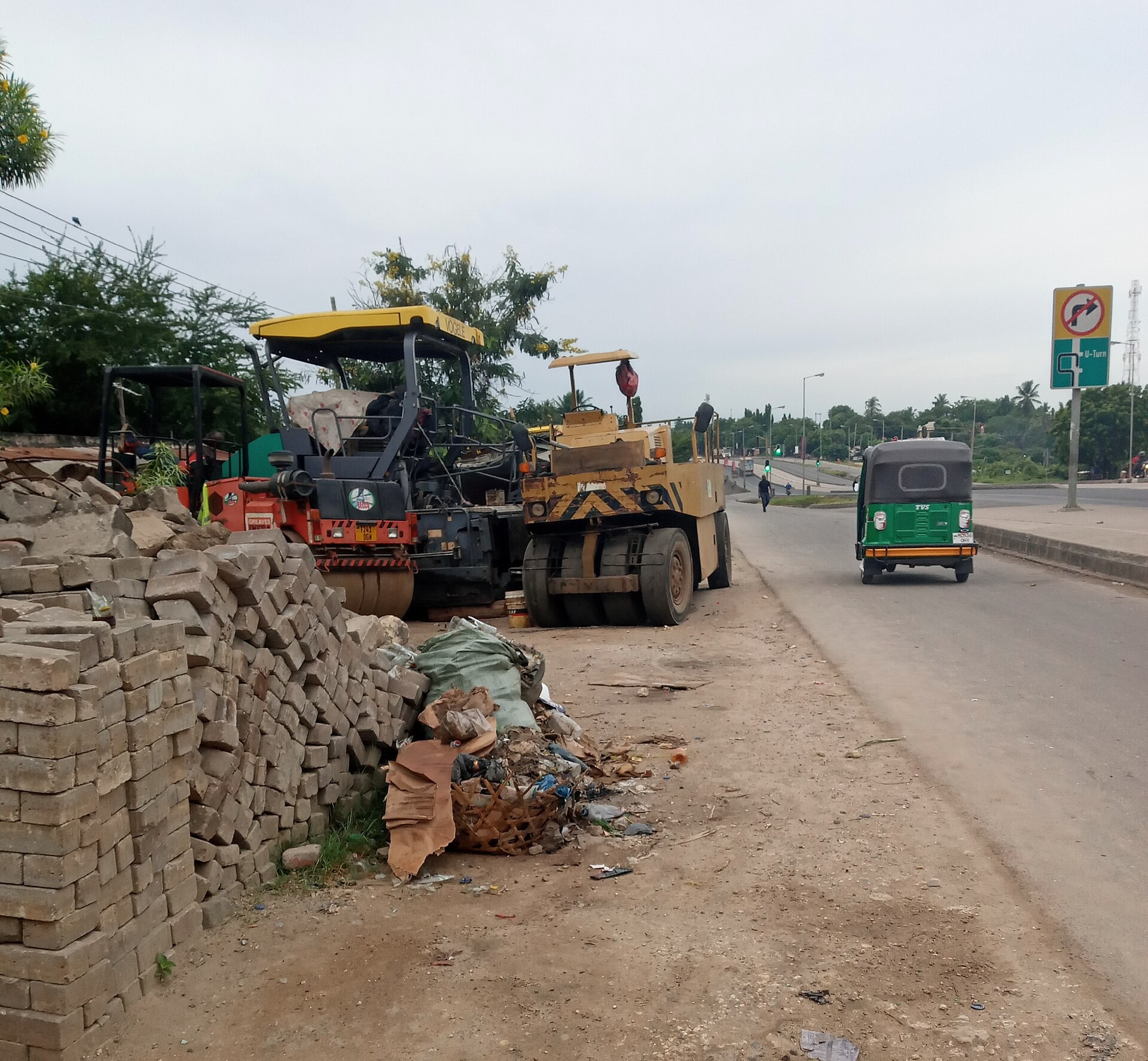 Road-building machines and stacked paving stones beside a road in Tanzania