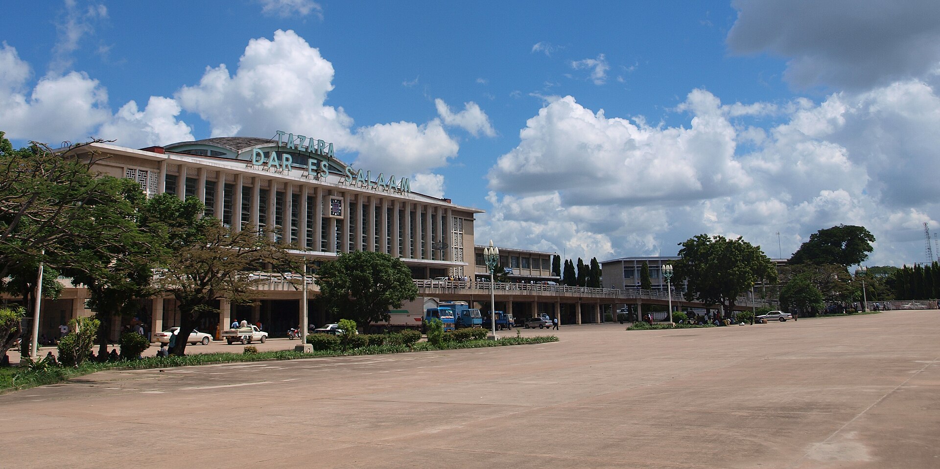The Tazara railway station in Dar es Salaam, a long low building with the station name on the roof, under a cloudy blue sky
