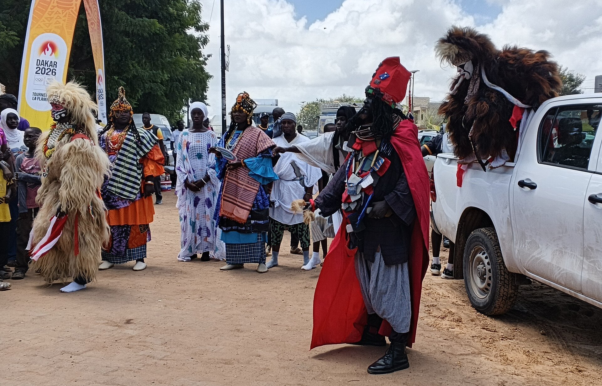Performers in traditional costumes and masks greeting the Dakar 2026 Youth Olympic flame relay in Diamniadio, Senegal