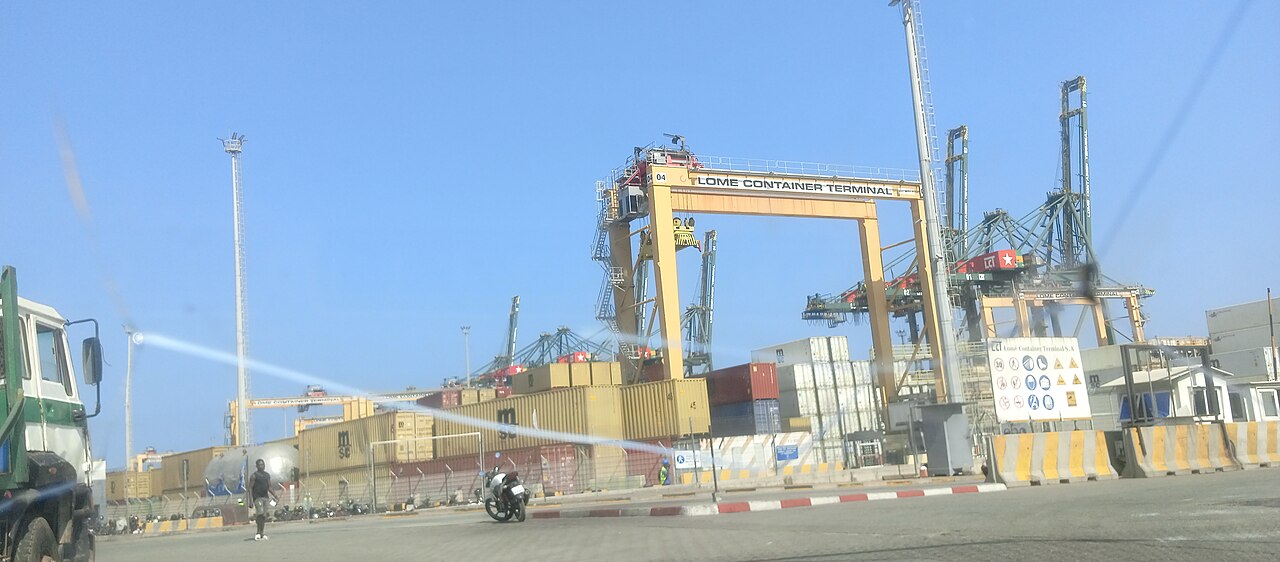 Cranes and stacked containers at the Lomé Container Terminal in Togo, with a motorbike and a pedestrian in the foreground