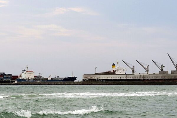 Container ships and quayside cranes at the port of Lomé, with waves breaking in the foreground.