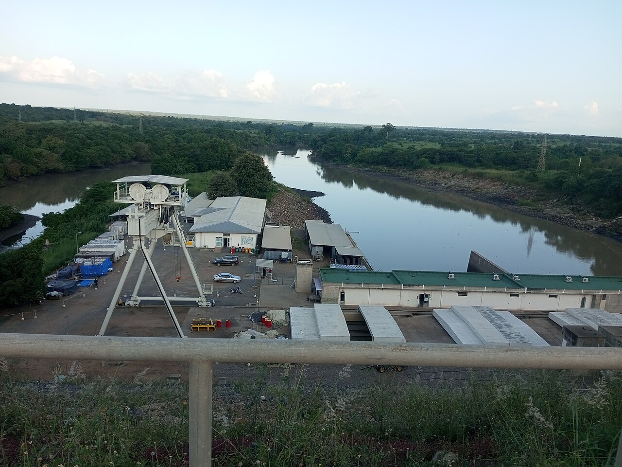 The Nangbéto hydroelectric dam on the Mono River, with a gantry crane, power station buildings and the river winding through green country.