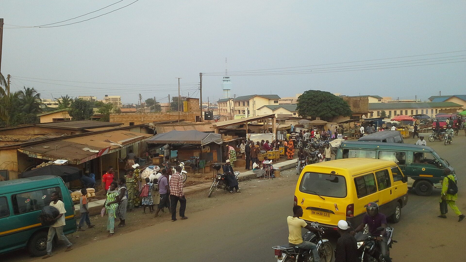 Minibuses, motorbikes and market stalls on a street in Aflao, the Ghanaian border town next to Togo, with a customs tower behind