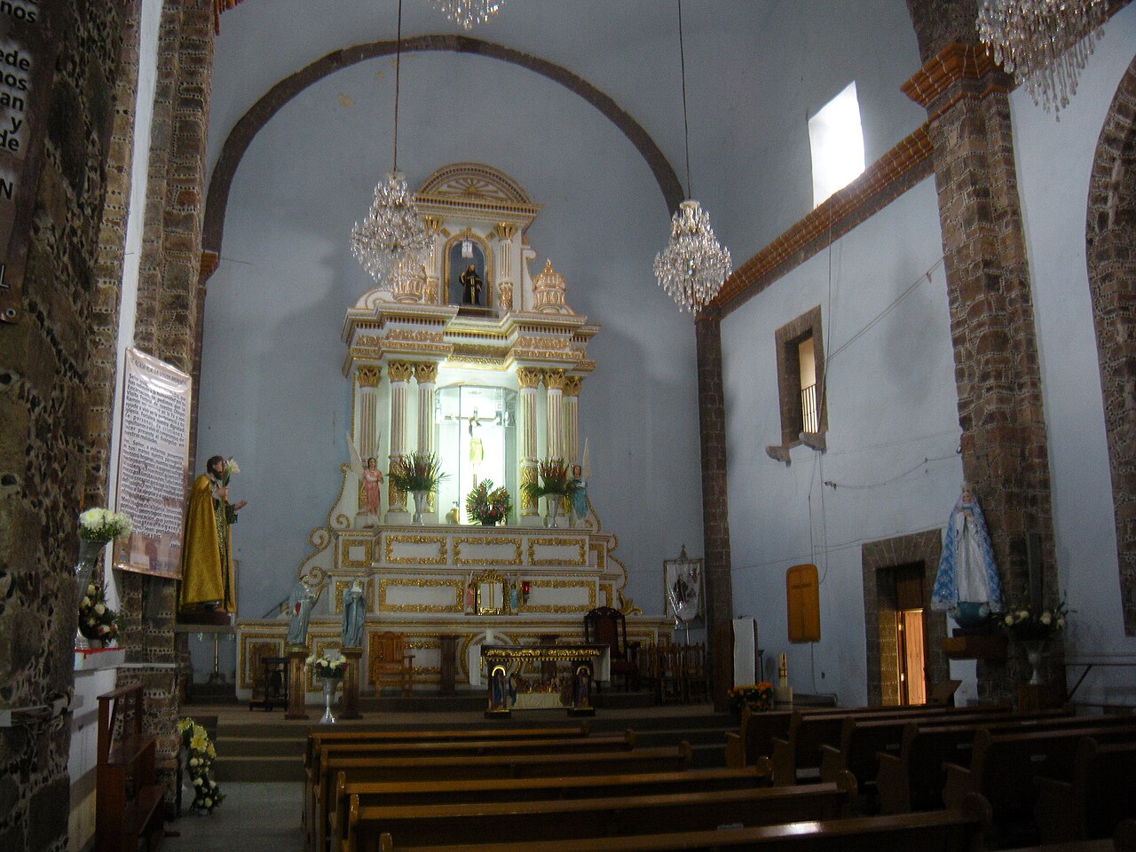 Interior of the San Guillermo convent church in Totolapan, Morelos, with a white and gold altarpiece, chandeliers and wooden pews