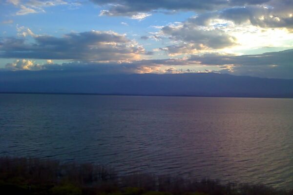 Calm water of Lago Enriquillo at dusk under a cloudy sky with mountains on the far shore