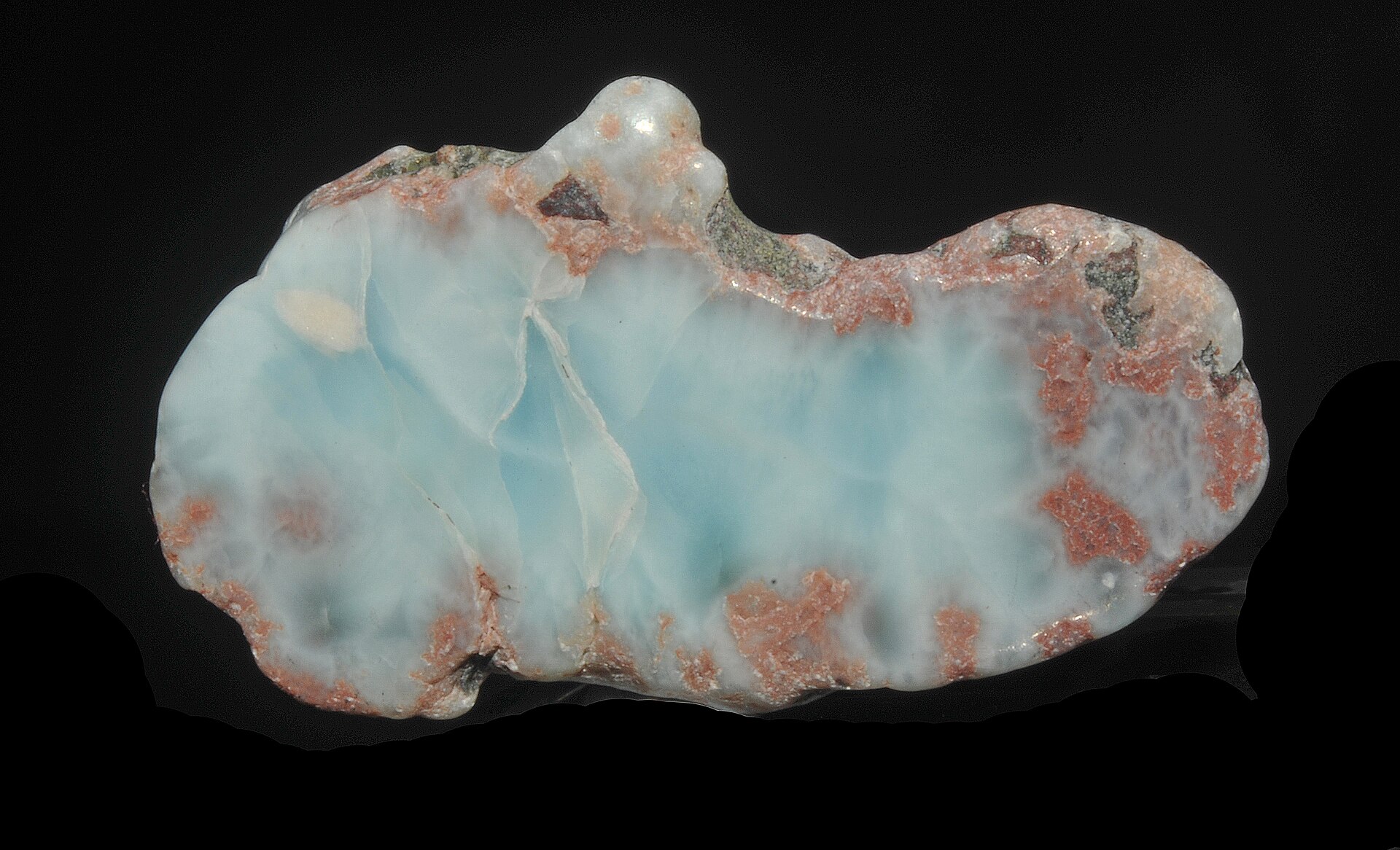 A polished pale blue larimar stone with reddish patches on a black background