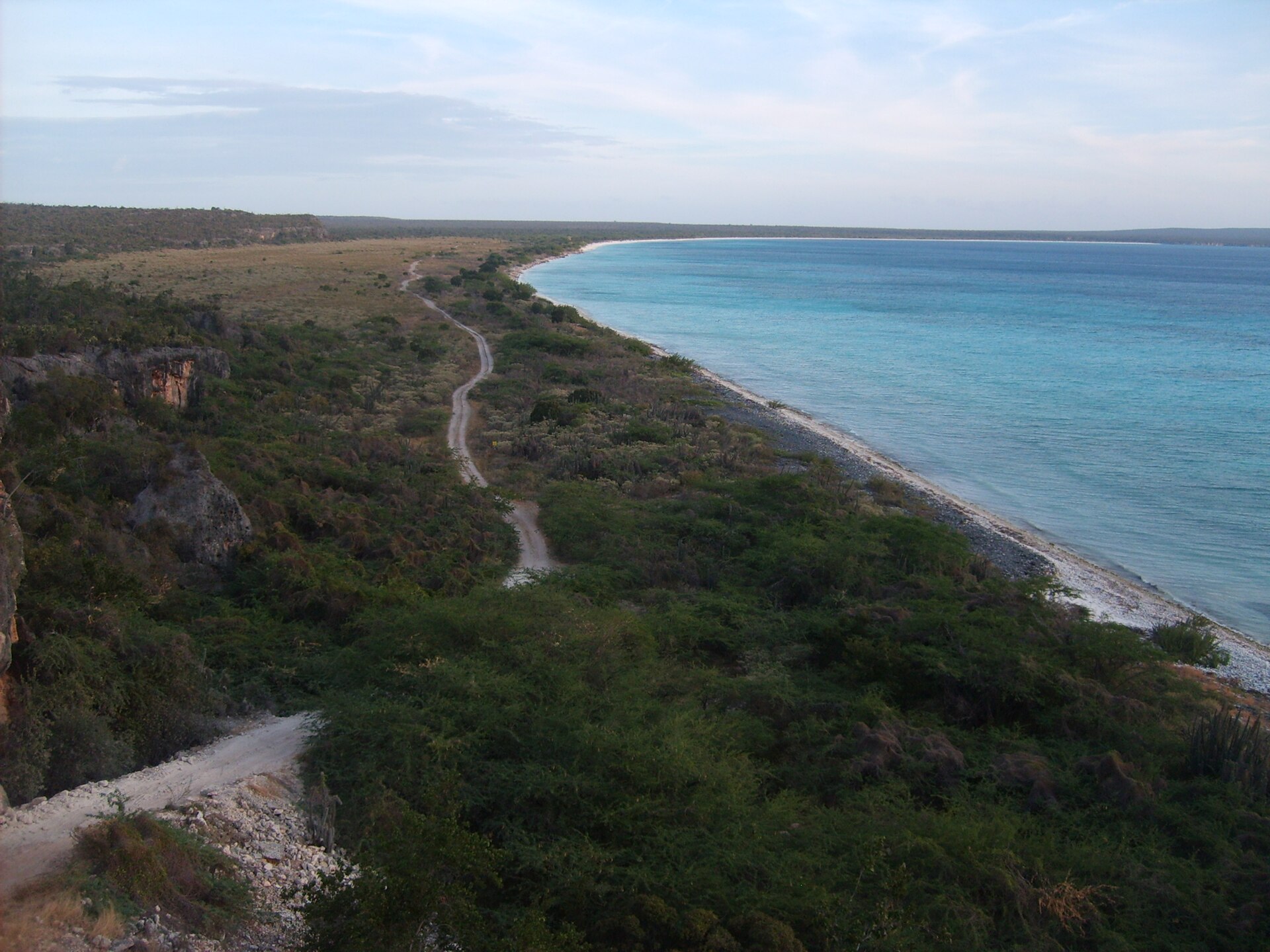 A dirt track along a scrub covered coast beside turquoise water at Bahia de las Aguilas