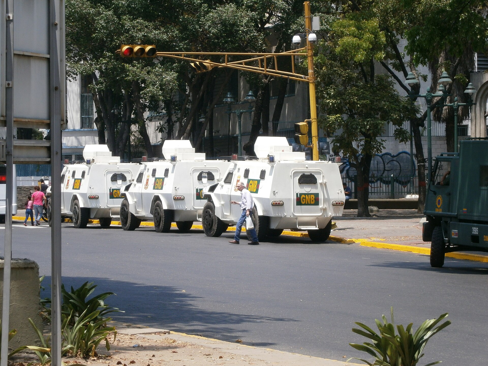 Three white armoured vehicles marked GNB parked in a row on a Caracas street, with a pedestrian walking past