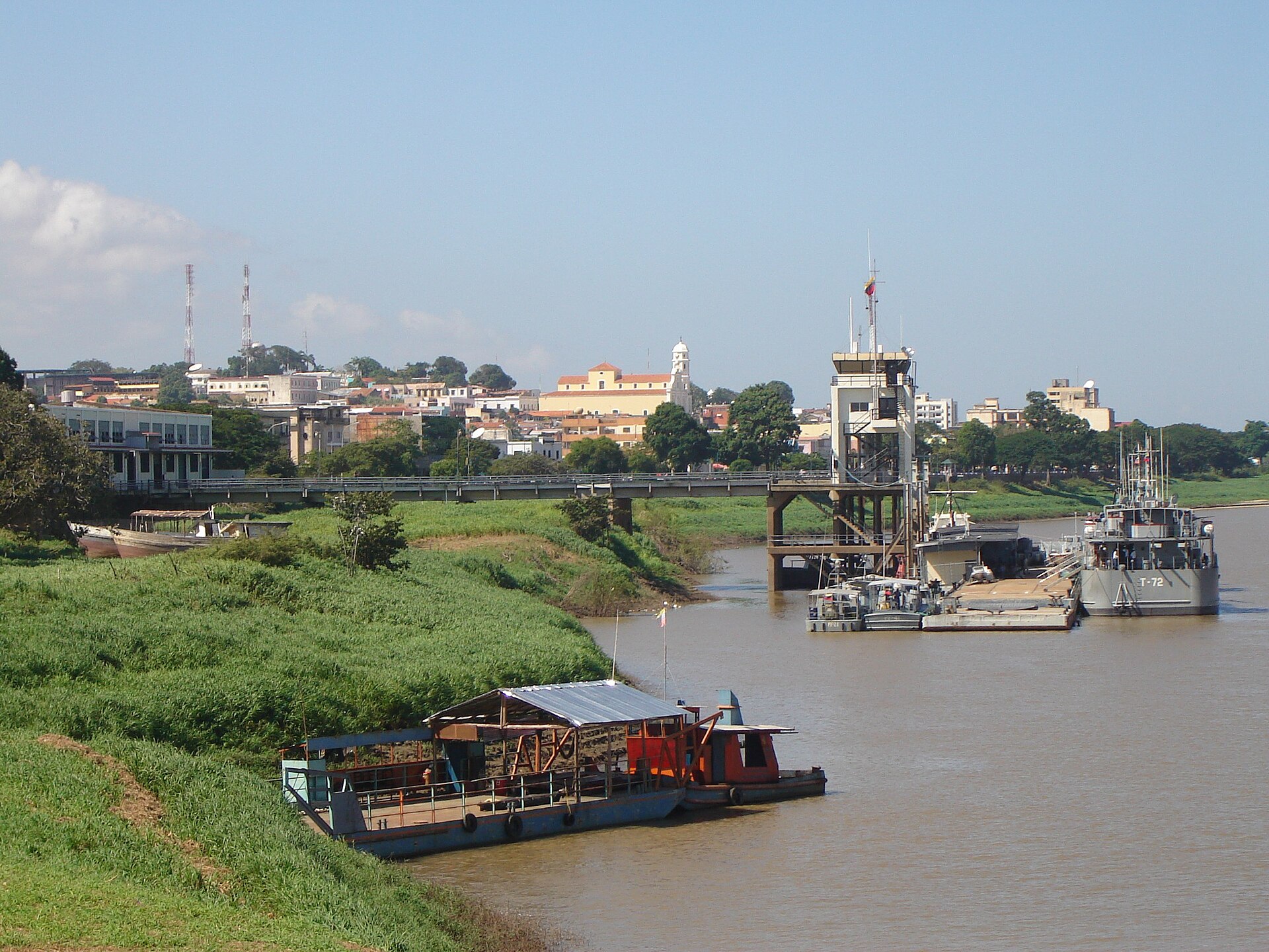 The Orinoco river at Ciudad Bolivar with a grey navy vessel at a pier, river boats and the town on the far bank