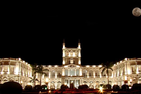 The floodlit white Palacio de López, the presidential palace in Asunción, at night with a full moon above and gardens in the foreground