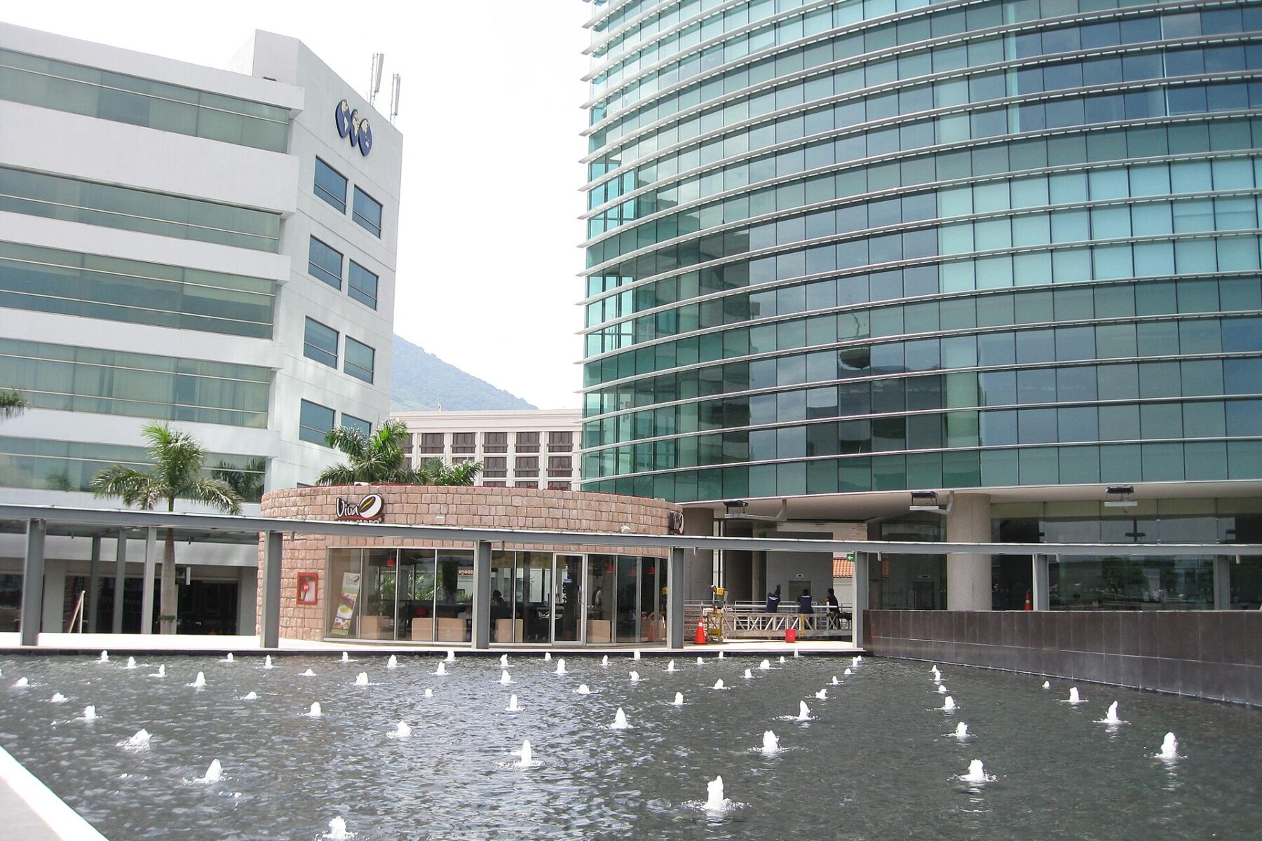 A fountain pool in front of glass office towers at Plaza Futura in San Salvador, with a green hill behind