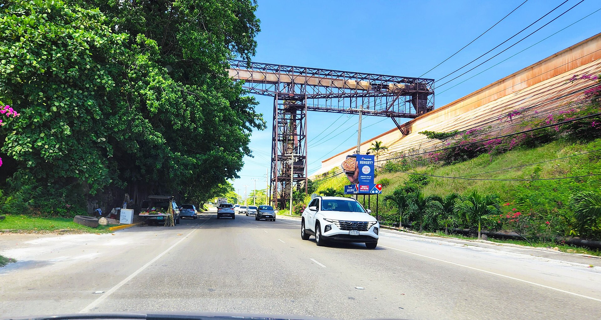 A steel gantry carrying a bauxite conveyor over a highway in St Ann Parish, with cars on the road