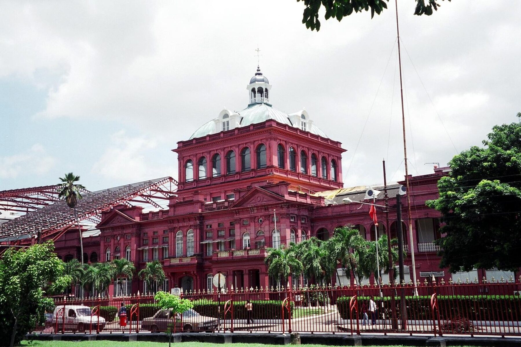 The red Victorian Red House government building in Port of Spain behind a railing, with palm trees in front