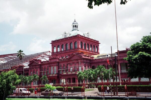 The red Victorian Red House government building in Port of Spain behind a railing, with palm trees in front