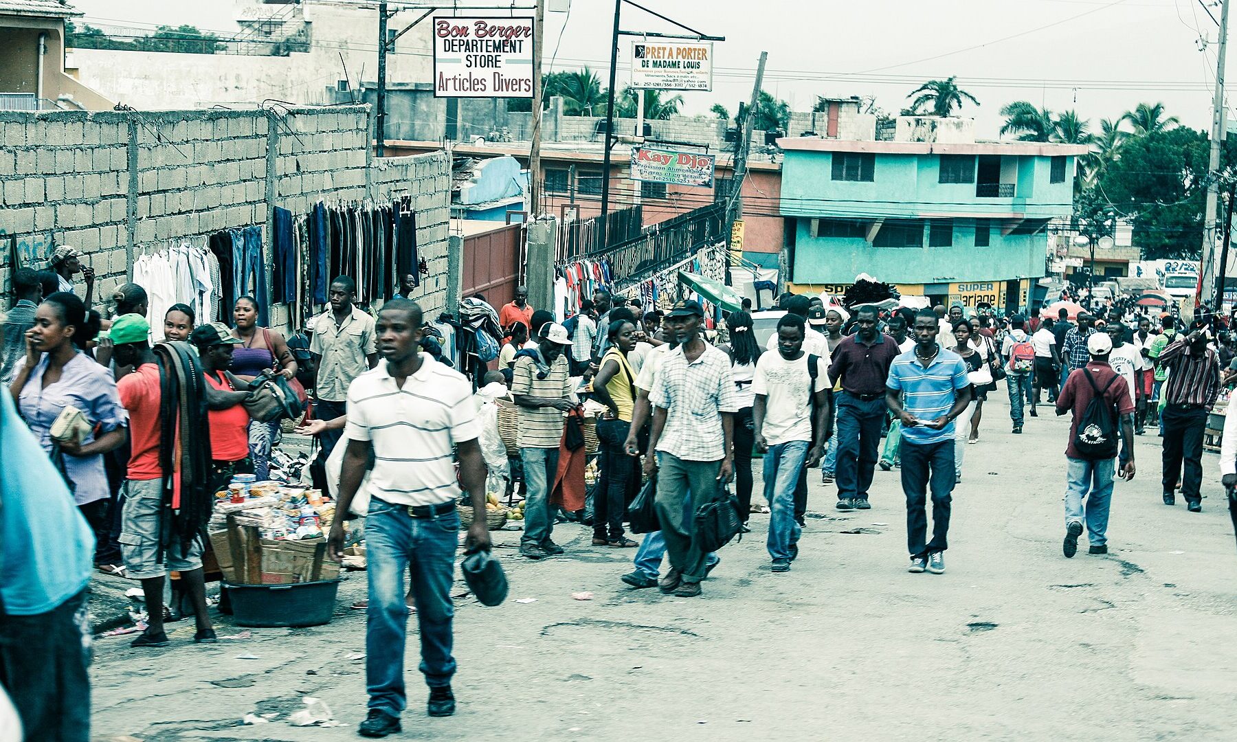 A busy street in Port-au-Prince, Haiti, with vendors selling clothes and pedestrians walking along a road lined with low buildings