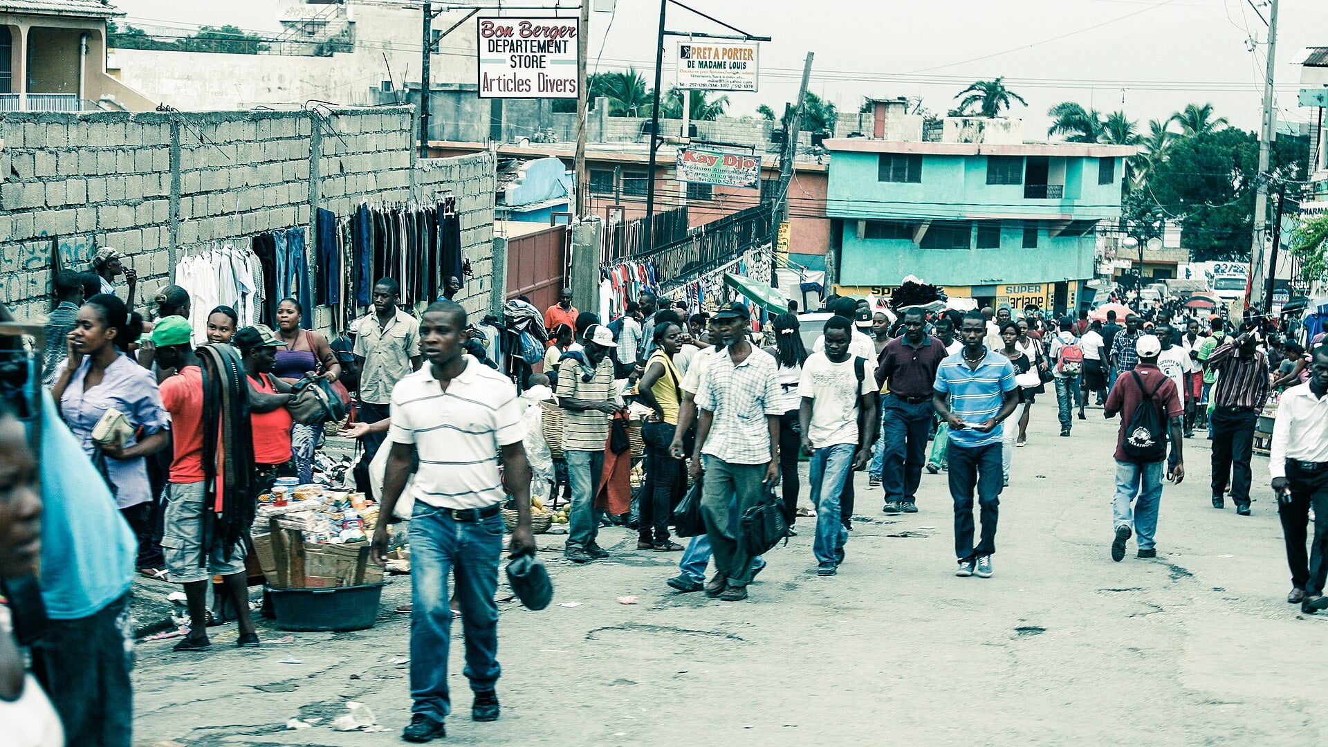 A busy street in Port-au-Prince, Haiti, with vendors selling clothes and pedestrians walking along a road lined with low buildings