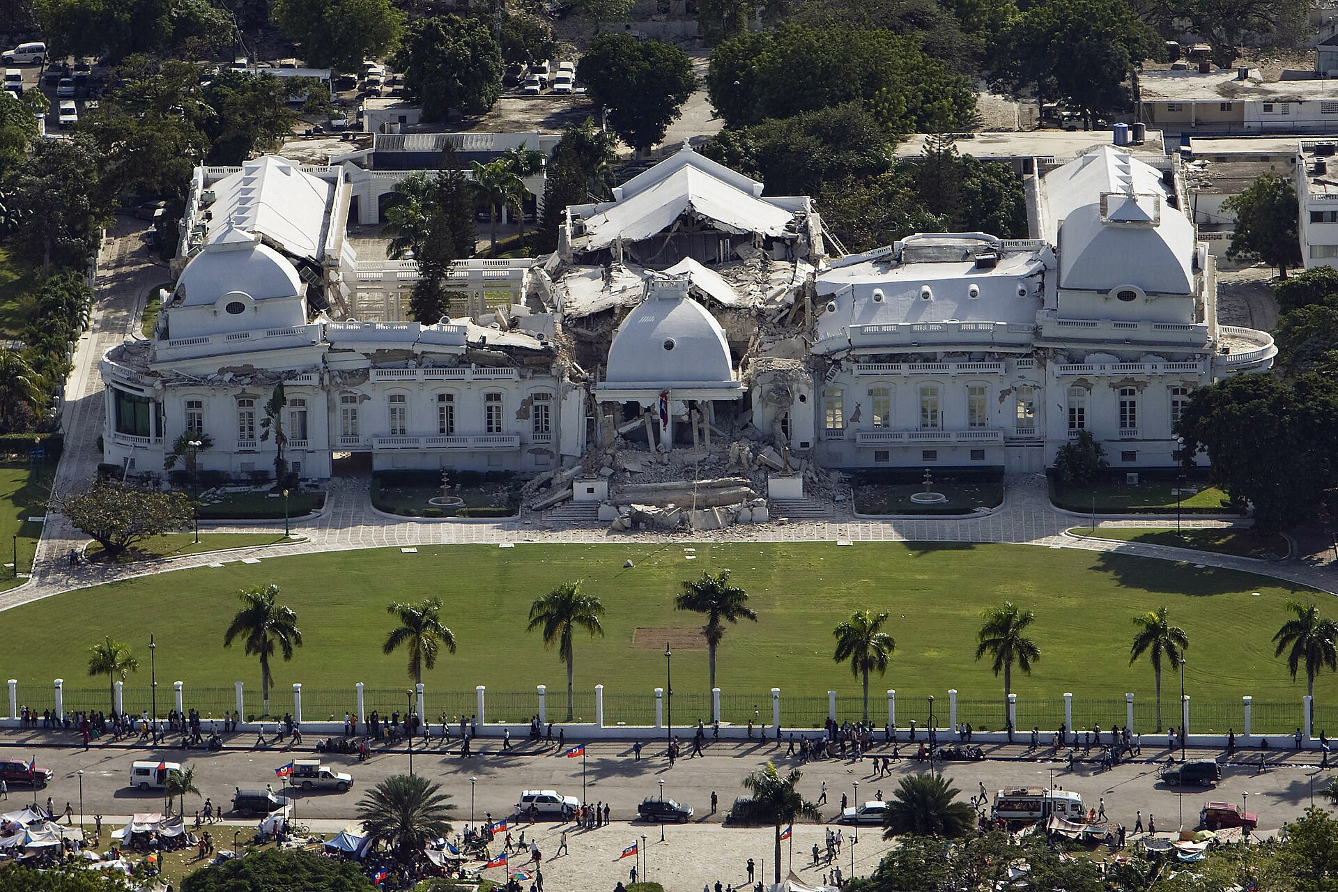 Aerial view of the collapsed centre of the National Palace in Port-au-Prince, with a lawn and crowds on the street in front
