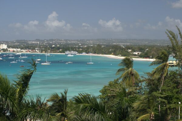 Turquoise Carlisle Bay with moored boats, a white beach and the Bridgetown coastline seen through palm trees