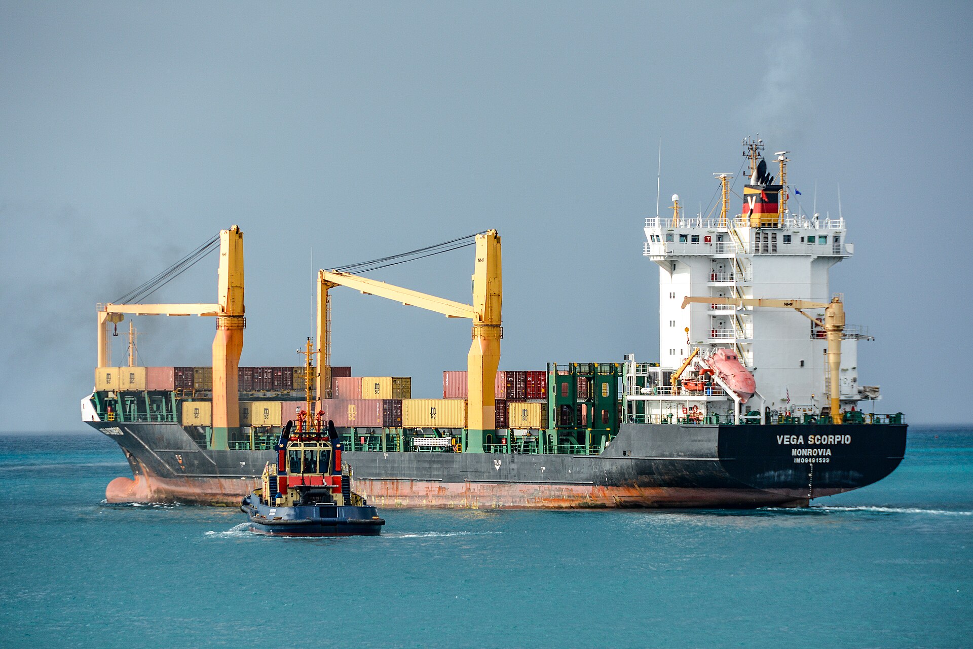 A small container ship and a tugboat on turquoise water leaving the harbour of Bridgetown, Barbados
