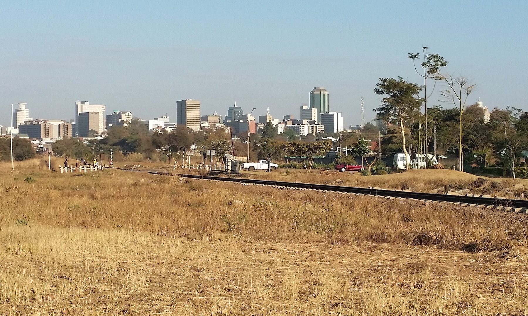 The Harare skyline seen across dry grass and a railway line under a clear sky