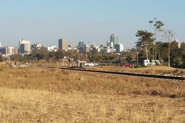 The Harare skyline seen across dry grass and a railway line under a clear sky