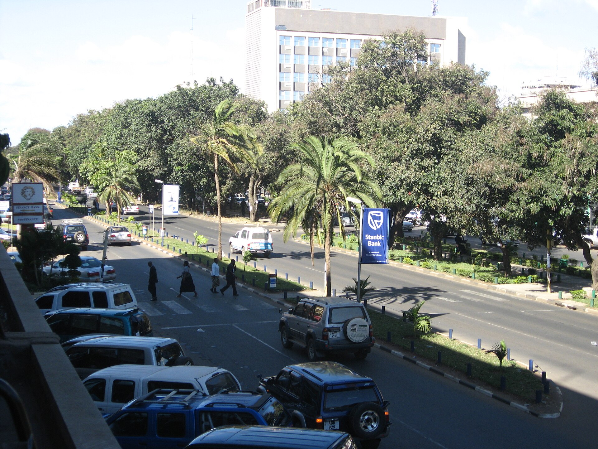 Cairo Road in Lusaka, a tree-lined avenue with palms, minibuses and parked cars, and an office tower in the background