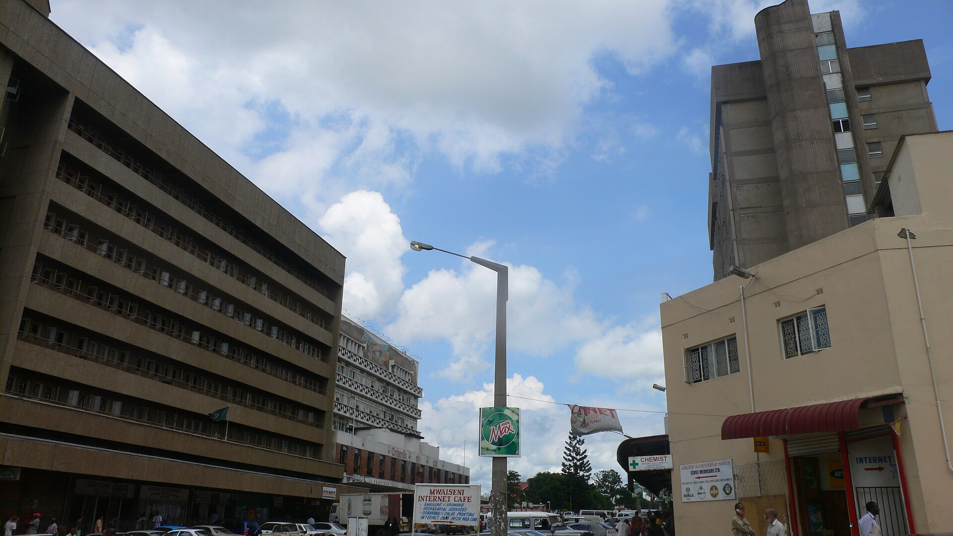 Office blocks and a street lamp in central Kitwe, Zambia, under a blue sky with clouds, with shops and an internet cafe sign at street level