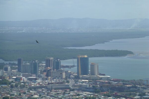 Aerial view of downtown Port of Spain with office towers beside the Gulf of Paria and hills behind.