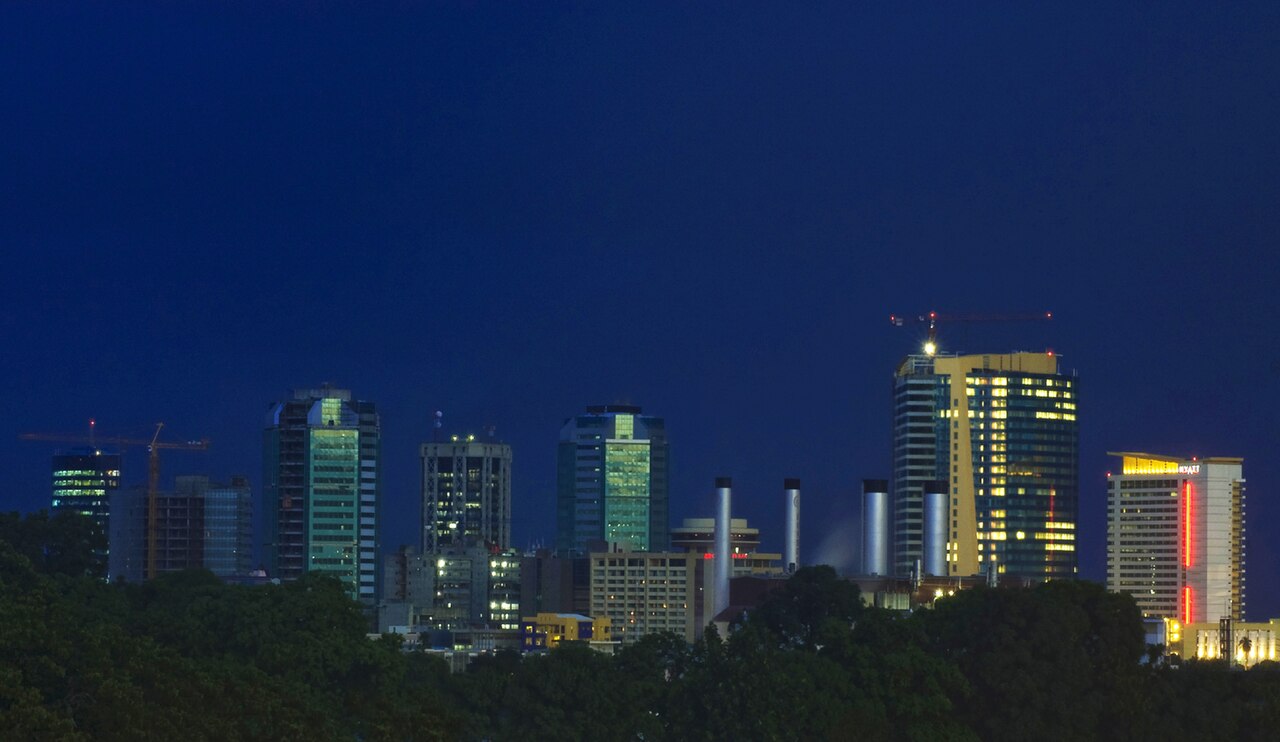 Lit office towers of Port of Spain's business district against a dark blue dusk sky