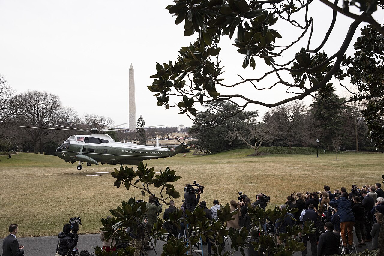 Reporters and camera crews watch the Marine One helicopter lift off from the White House South Lawn